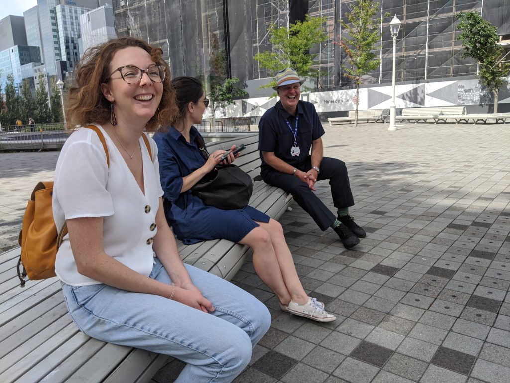 Deux jeunes femmes sont assises sur un banc dans le Vieux Montréal avec leur guide professionnel portant son permis de la Ville de Montréal